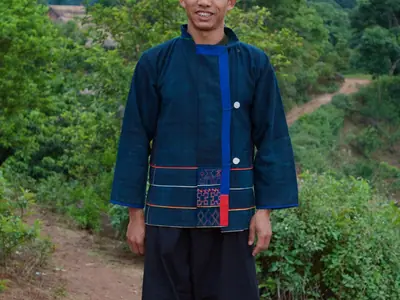 Een Akha-man in donkere traditionele kleding op een dorpspad in Thailand