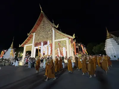 Procession of monks in orange robes in front of the lit-up hall of Wat Chedi Luang in Chiang Mai on Asalha Puja night (2026)