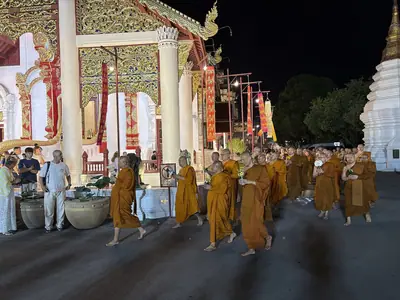 Monks walking past a gathering of laypeople with offerings at Wat Chedi Luang on Asalha Puja 2026