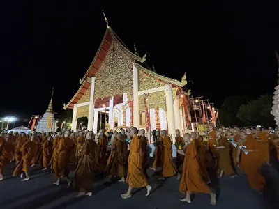 Monks gathered in front of the golden-lit hall of Wat Chedi Luang at night during Asalha Puja