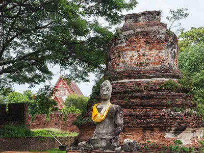 A seated Buddha statue in front of a ruined brick tower at Wat Phra Si Sanphet
