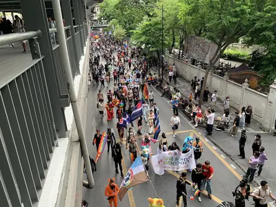 Participants marching with banners along a tree-lined road at Bangkok Pride 2024