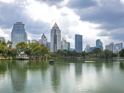 Lumphini Park's lake with skyscrapers behind and a cloudy sky