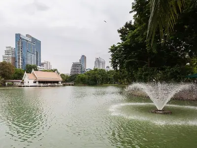 A fountain on the lake in Lumphini Park with the city skyline beyond