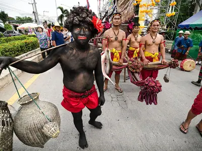 Een man bedekt met zwarte verf leidt gekostumeerde dansers in de optocht van het Yasothon Rocket Festival op 11 mei 2013