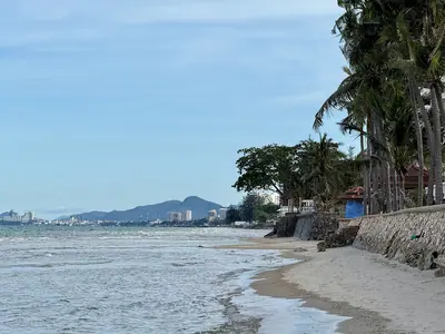 Uitzicht vanaf het strand van Cha-am richting Hua Hin met palmbomen, zee en bergen in de verte