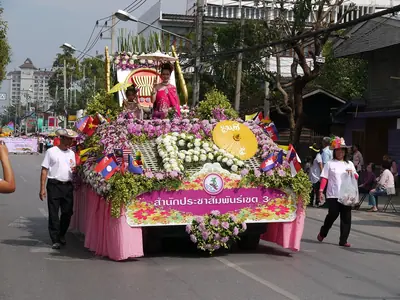 Een roze-gele bloemenwagen met een versierde luifel in de optocht van het Chiang Mai Flower Festival