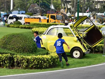 Een kind speelt bij een gele speelgoedauto op het gazon tijdens het Kinderdag-evenement bij Government House