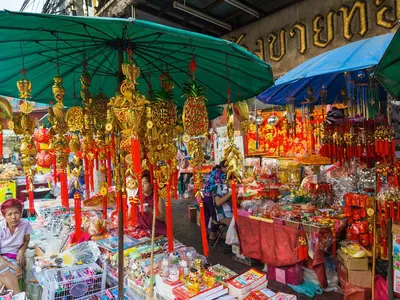 Golden figurines and lucky charms on a Chinese New Year stall under a red umbrella on Yaowarat Road (2016)