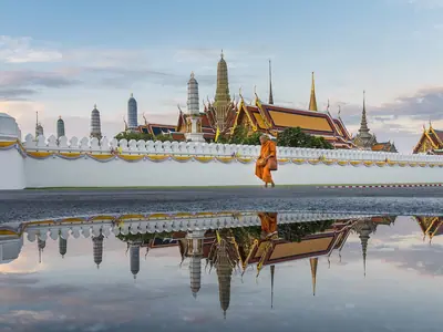 Tempel van de Smaragdgroene Boeddha (Wat Phra Kaew) weerspiegeld in een plas bij schemering, met een voorbijlopende monnik