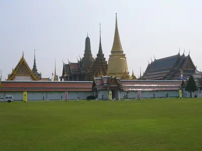 Wat Phra Kaew en het Grote Paleis gezien vanaf het gazon: gouden chedi's en daken met meerdere lagen