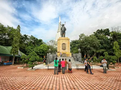 Visitors on the brick plaza of the Don Chedi Monument with the statue and white chedi behind