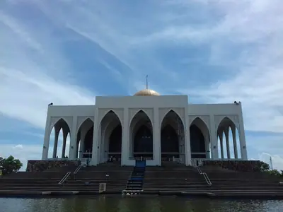 Songkhla Central Mosque: a white building with a row of arches on a pond, under a blue sky