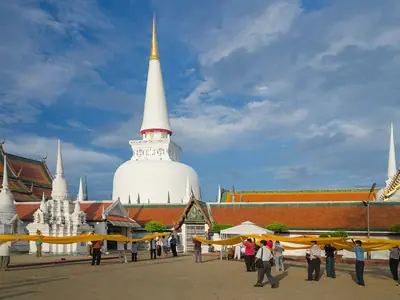 The white Phra Borom That chedi of Wat Phra Mahathat Woramahawihan in Nakhon Si Thammarat with visitors in the courtyard