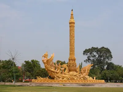 Tall wax candle sculpture on a boat-shaped base in Ubon Ratchathani, seen across a green park