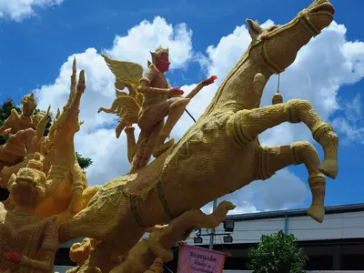 Golden wax sculpture of a winged figure and horse against a blue sky at the Ubon Candle Festival parade