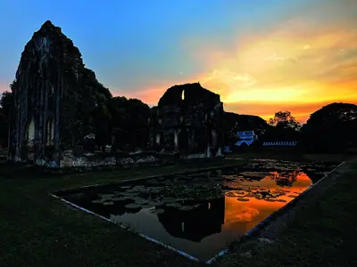 Ruins of Narai Ratchaniwet at sunset with reflections in a puddle