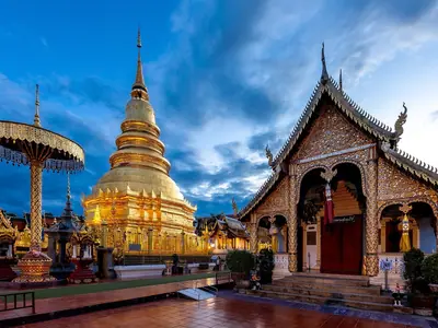 Wat Phra That Hariphunchai in Lamphun at dusk: a golden chedi and temple hall under a blue sky