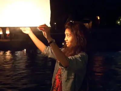 A woman releasing a glowing paper lantern over the water during the Krathong Festival in Chiang Mai
