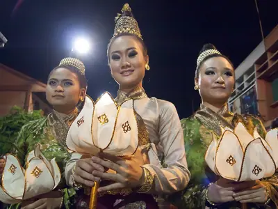 Women in Lanna costumes with golden headdresses carry lotus-shaped lanterns in a Chiang Mai procession at night