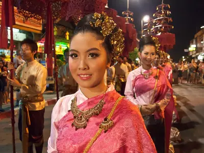 A woman in a pink Lanna costume with an ornate golden headdress in a Chiang Mai procession at night