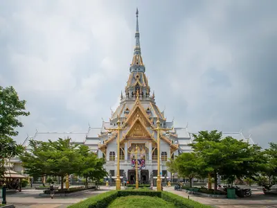 The ornate white Luang Po Sothon chapel with a tiered spire and a garden in front