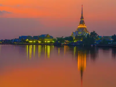 Wat Sothon Wararam Woraviharn glowing orange at dusk, reflected in the river