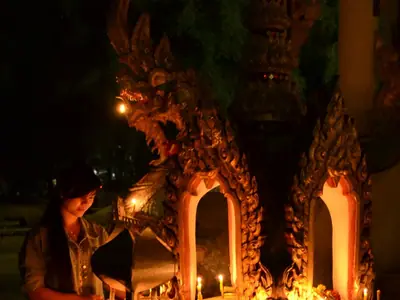 Devotees with candles inside a dark temple doorway at Wat Khung Taphao on Magha Puja day