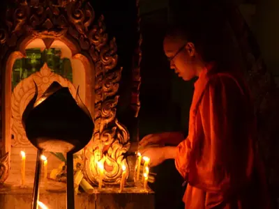 A monk lights candles at an altar at night during Magha Puja at Wat Khung Taphao