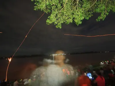 Red fireballs streak up from the Mekong River at night while crowds watch from the bank