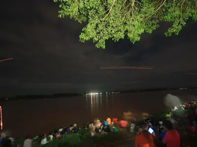 Glowing fireballs rising over the Mekong at night with a crowd on the shore