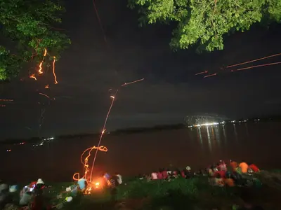 A fireball rises from the dark river at night beneath overhanging trees