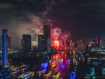Fireworks above the glowing Bangkok skyline reflected in the river on New Year's night