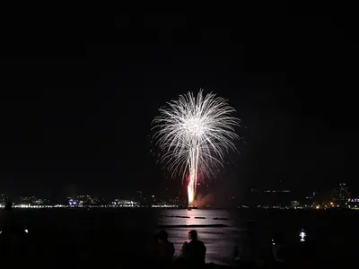 A white firework bursts over Pattaya Bay with the shoreline lights below (28 November 2020)