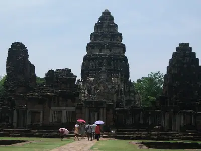 The towers of Phimai sanctuary rising above the ruins with visitors holding umbrellas