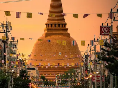 The golden Phra Pathom Chedi at the end of a street in Nakhon Pathom, with a monk walking in orange robes