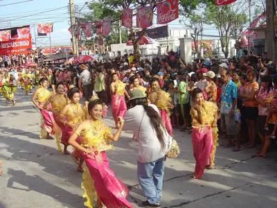 Deelnemers in gele en roze kostuums dansen in de Songkran-optocht in Phra Pradaeng
