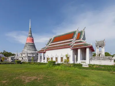 Temple hall and the red-and-white chedi of Wat Phra Samut Chedi seen across a lawn