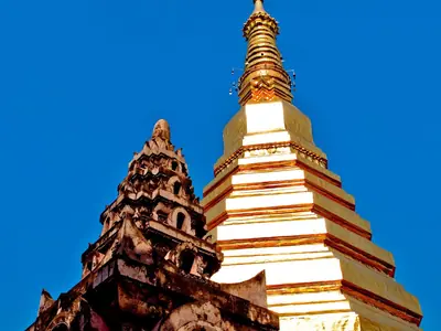 The golden chedi and a red roof at Wat Phra That Cho Hae in Phrae Province against a blue sky