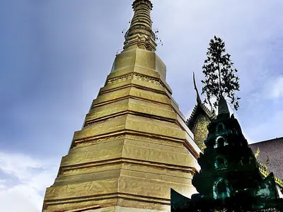The golden chedi of Wat Phra That Cho Hae rising over trees in Phrae