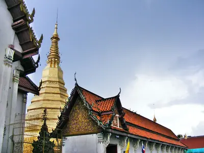 The golden chedi and temple roofs of Wat Phra That Cho Hae under a cloudy sky