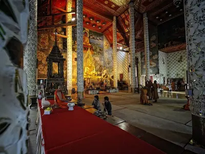 Interior of the wihan at Wat Phra That Cho Hae with a golden Buddha image and red carpet