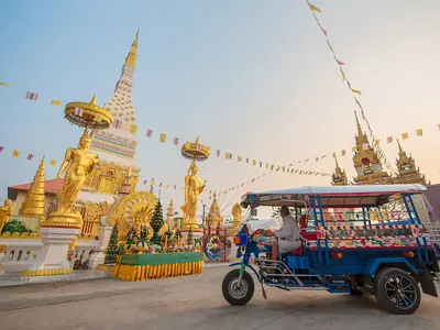A tuk-tuk passes below the golden Wat Phra That Phanom chedi decorated with flags
