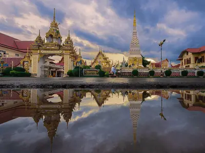 Wat Phra That Phanom with its tall chedi and temple buildings reflected in a pool