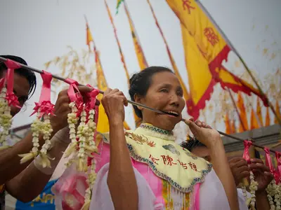 A participant in the Phuket Vegetarian Festival procession with ceremonial skewers through the cheeks, holding flags