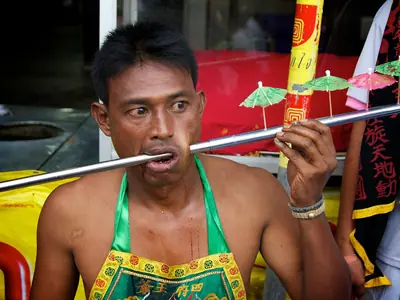 A devotee with a long rod through both cheeks and small umbrellas at the Phuket Vegetarian Festival