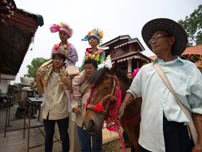 Boys in festive costume and flower headdresses with adults in a street during the Poi Sang Long festival