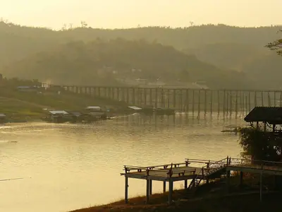 The long wooden Mon Bridge across the water at Sangkhlaburi in golden evening light