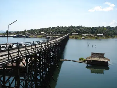 The wooden Mon Bridge curving across the lake in Sangkhlaburi with a floating house