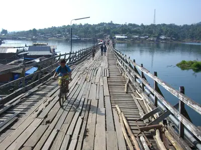 A person walking along the wooden planks of the Mon Bridge in Sangkhlaburi